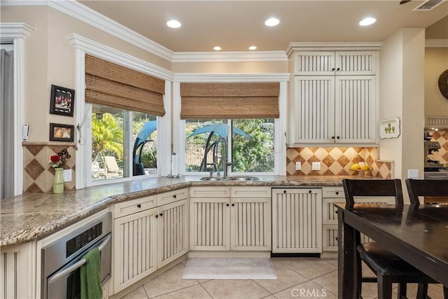 kitchen with a sink, cream cabinets, stainless steel oven, and crown molding