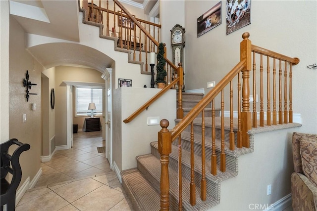 staircase with arched walkways, baseboards, and tile patterned floors