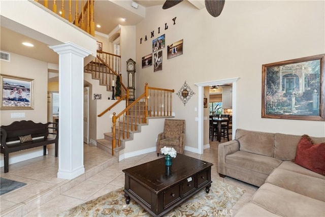 living area featuring light tile patterned floors, visible vents, a towering ceiling, stairway, and ornate columns