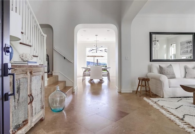 foyer featuring arched walkways, crown molding, baseboards, and stairs