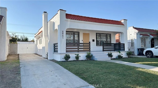 mediterranean / spanish-style home with a porch, a gate, a front yard, and stucco siding