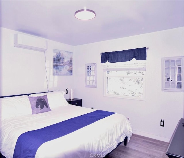 bedroom featuring a wall unit AC, baseboards, and wood finished floors