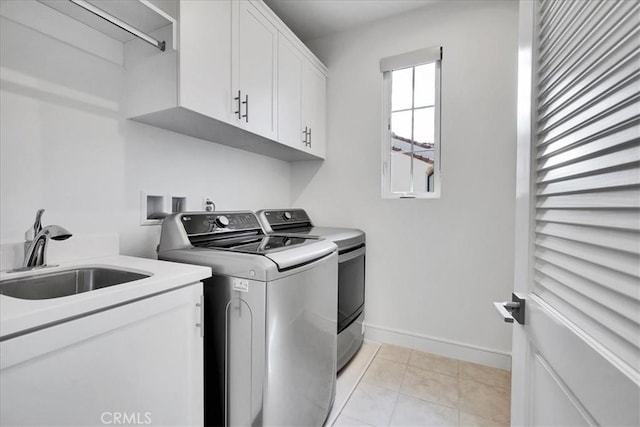 laundry area featuring washing machine and clothes dryer, light tile patterned floors, cabinet space, a sink, and baseboards