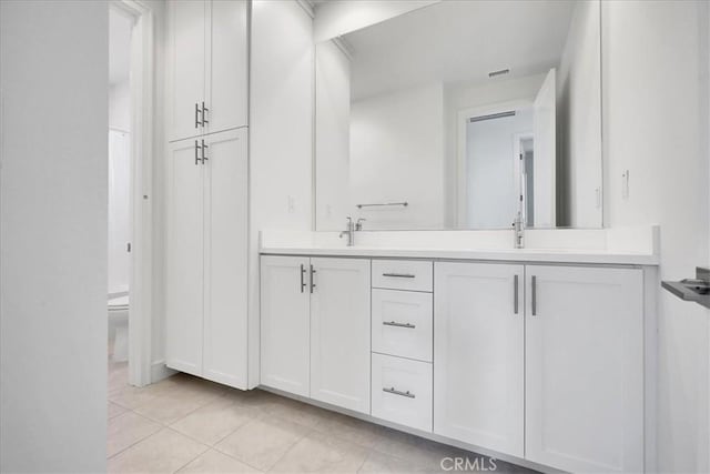 bathroom featuring toilet, a sink, visible vents, tile patterned floors, and double vanity