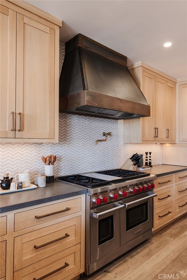 kitchen featuring light wood-style flooring, double oven range, wall chimney range hood, decorative backsplash, and dark countertops