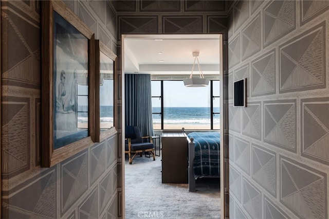 corridor featuring a view of the beach, light colored carpet, and a water view