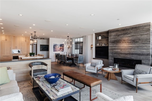 living room with a chandelier, a large fireplace, light wood finished floors, and recessed lighting