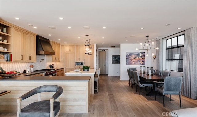 kitchen featuring high end stainless steel range, a peninsula, decorative light fixtures, built in microwave, and wall chimney range hood