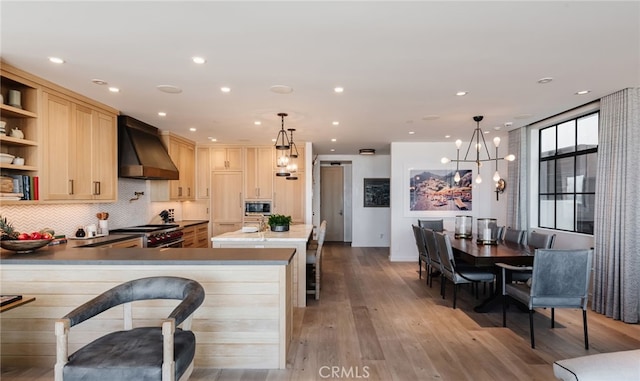 kitchen with exhaust hood, light brown cabinets, light wood-style floors, stainless steel appliances, and backsplash
