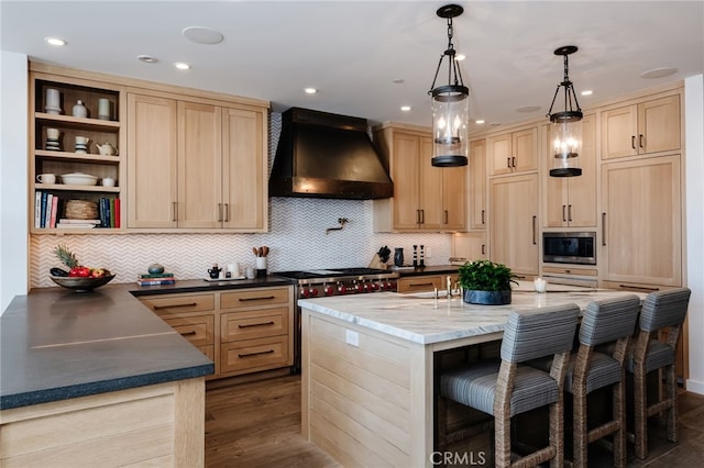 kitchen with stainless steel microwave, a breakfast bar, an island with sink, premium range hood, and light brown cabinetry