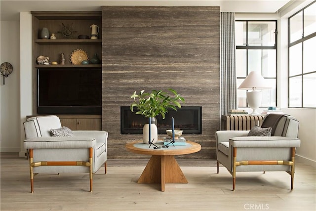 sitting room featuring light wood-type flooring, a wealth of natural light, baseboards, and a premium fireplace