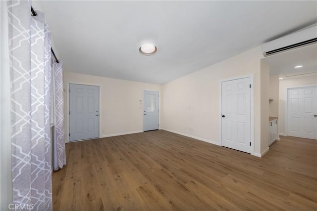 empty room with vaulted ceiling, baseboards, dark wood-type flooring, and an AC wall unit