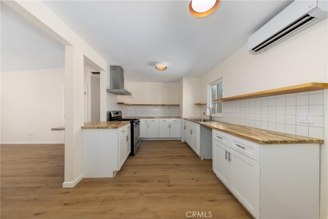 kitchen with a wall unit AC, stainless steel range oven, wall chimney exhaust hood, and white cabinetry