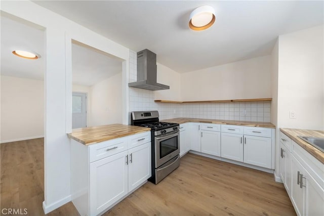 kitchen with decorative backsplash, wall chimney exhaust hood, butcher block countertops, white cabinetry, and stainless steel range with gas stovetop