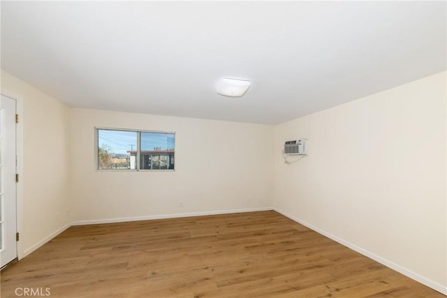 empty room with an AC wall unit, baseboards, and wood finished floors