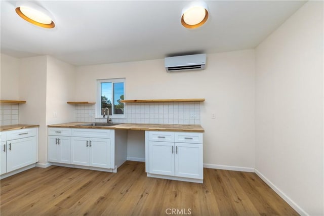 kitchen with white cabinets, wooden counters, a sink, and a wall mounted AC