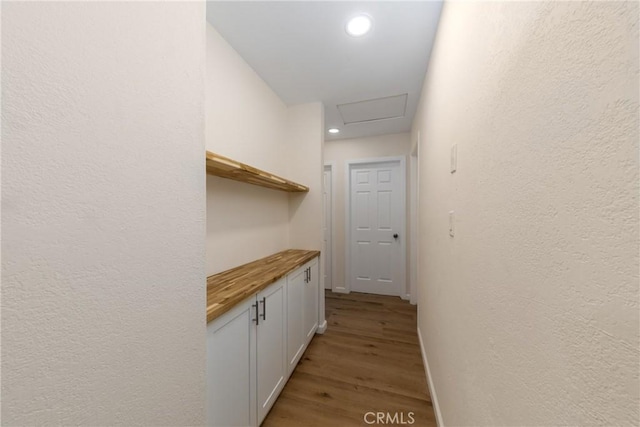 corridor with recessed lighting, a textured wall, attic access, light wood-style floors, and baseboards