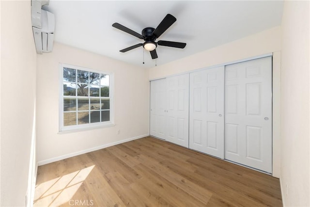 unfurnished bedroom featuring a closet, a ceiling fan, light wood-type flooring, a wall mounted air conditioner, and baseboards