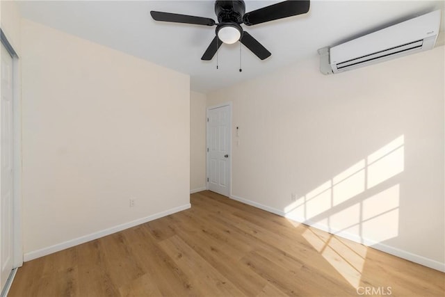 unfurnished room with ceiling fan, a wall mounted AC, light wood-type flooring, and baseboards