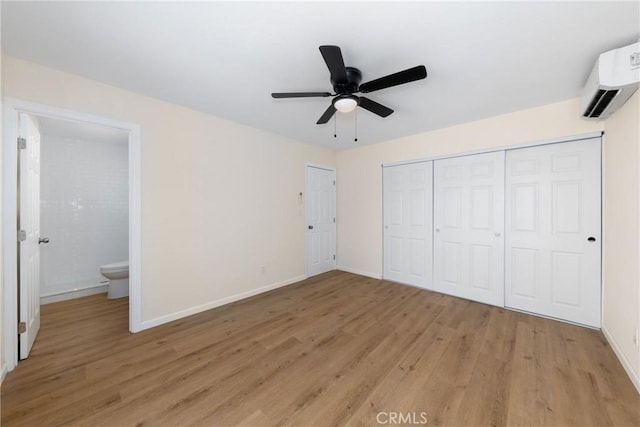 unfurnished bedroom with light wood finished floors, a closet, a wall unit AC, and baseboards