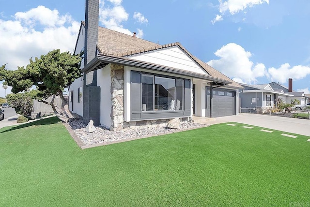 view of front facade with a chimney, a shingled roof, concrete driveway, an attached garage, and a front yard