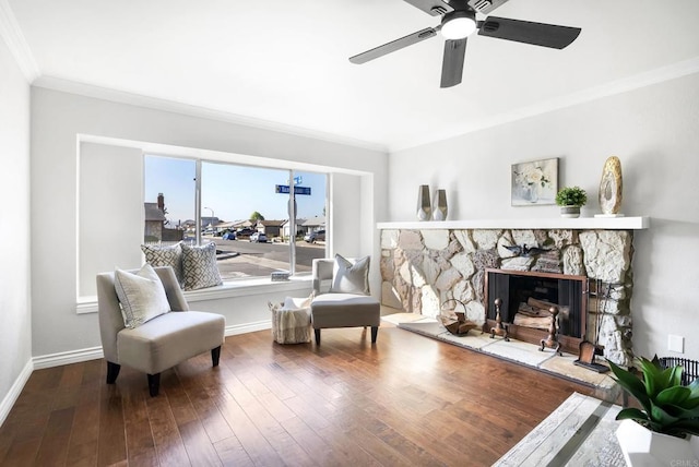 sitting room with hardwood / wood-style flooring, baseboards, ornamental molding, and a stone fireplace