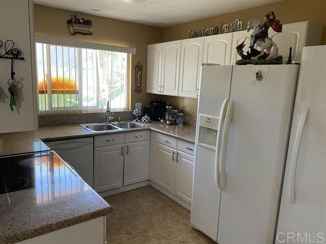 kitchen featuring light tile patterned floors, light stone counters, white appliances, a sink, and white cabinetry