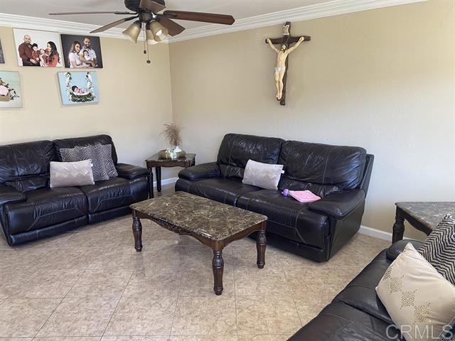 living area with ceiling fan, ornamental molding, and baseboards