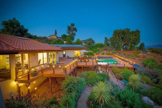 back of house with a tiled roof, a deck, solar panels, and stucco siding