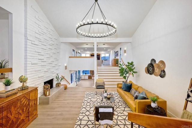 living room featuring stairway, wood finished floors, a stone fireplace, a towering ceiling, and an inviting chandelier