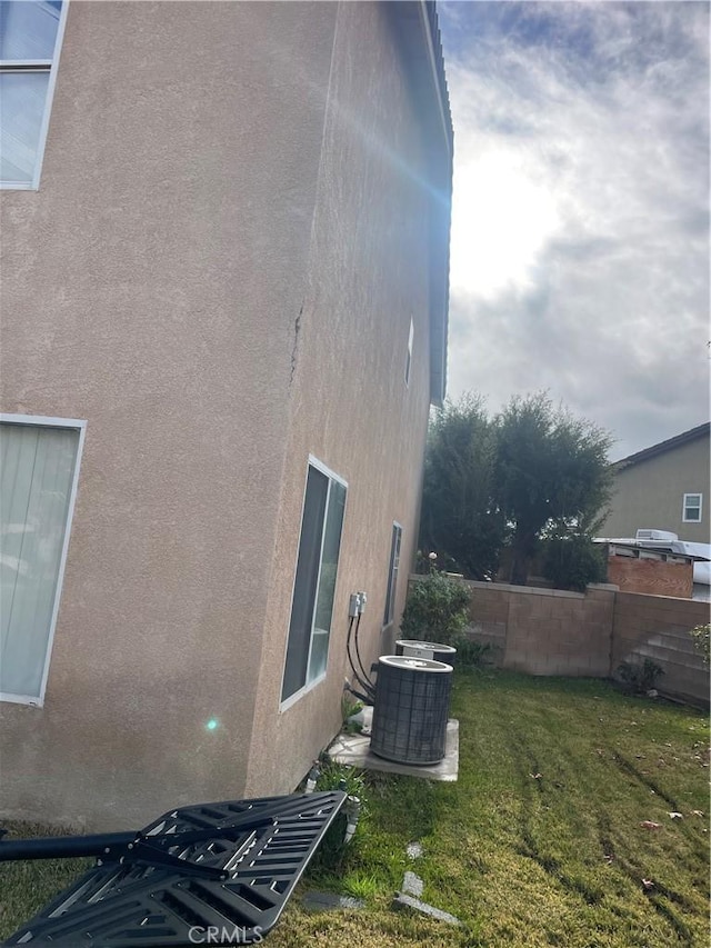 view of home's exterior featuring stucco siding, a yard, central AC unit, and fence