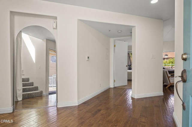hallway with stairway, baseboards, arched walkways, and dark wood-type flooring