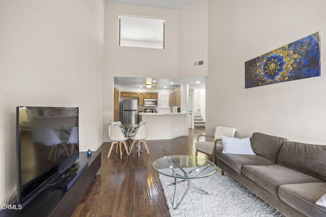 living area with dark wood-style floors, visible vents, a towering ceiling, and stairs