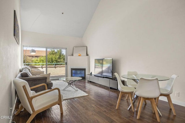 living room featuring high vaulted ceiling, dark wood-type flooring, a glass covered fireplace, and baseboards