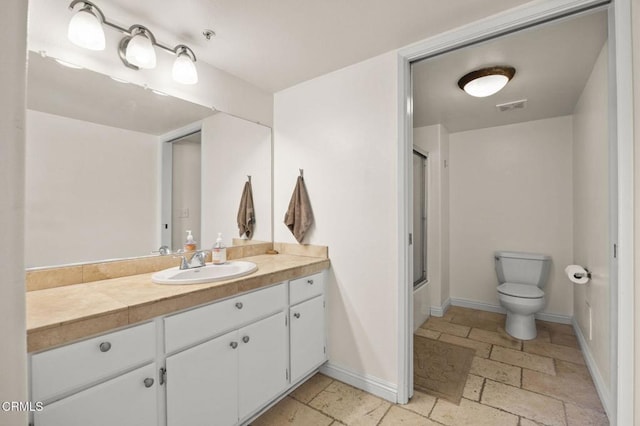 bathroom with stone tile floors, vanity, baseboards, visible vents, and combined bath / shower with glass door