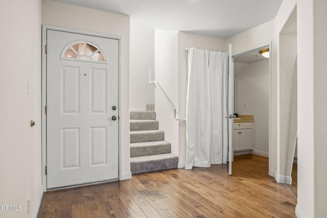 foyer entrance with light wood finished floors, baseboards, and stairway