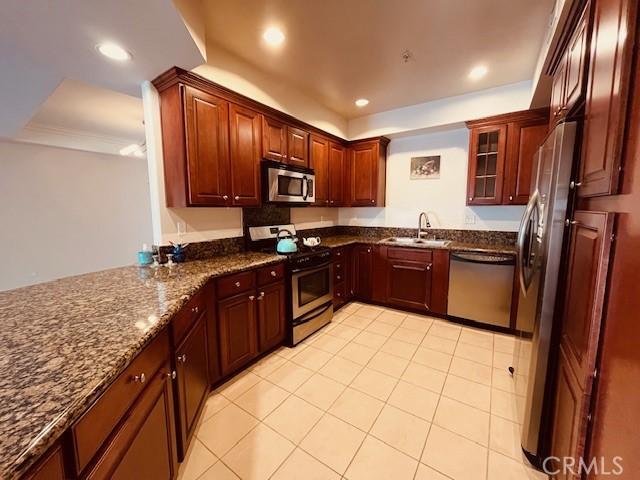 kitchen with dark stone countertops, recessed lighting, a sink, stainless steel appliances, and glass insert cabinets