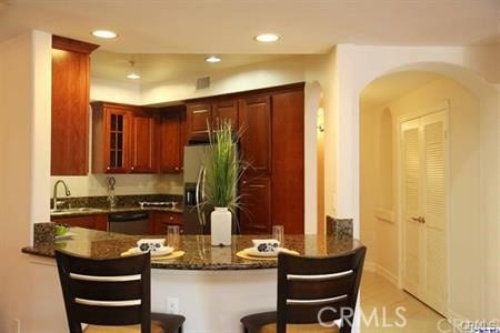 14242 Burbank Blvd Unit 103, Sherman Oaks, CA 91401 - kitchen featuring a peninsula, arched walkways, glass insert cabinets, appliances with stainless steel finishes, and dark stone countertops