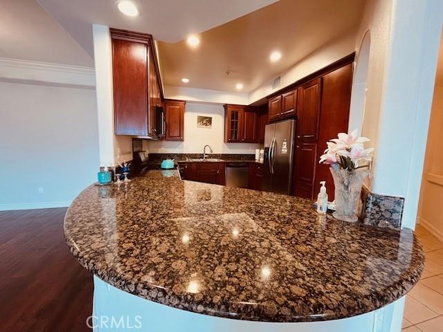 14242 Burbank Blvd Unit 103, Sherman Oaks, CA 91401 - kitchen with appliances with stainless steel finishes, a peninsula, dark stone counters, a sink, and glass insert cabinets
