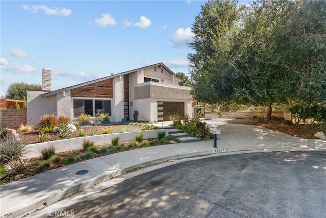 view of front of property featuring driveway, a balcony, a chimney, an attached garage, and stucco siding