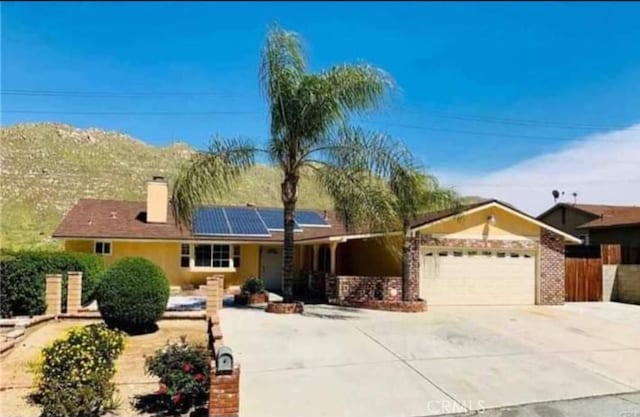 single story home featuring driveway, solar panels, a chimney, an attached garage, and fence