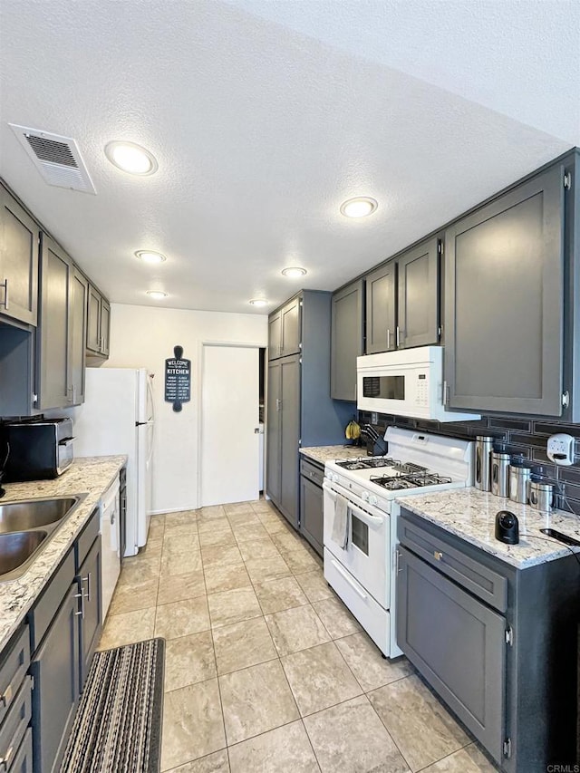 kitchen with white appliances, visible vents, gray cabinets, a textured ceiling, and a sink