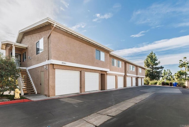 view of property exterior with stairs, community garages, and stucco siding