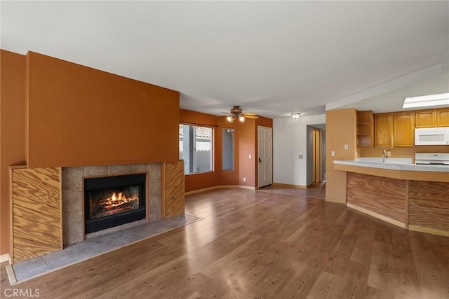 unfurnished living room featuring ceiling fan, baseboards, wood finished floors, and a tiled fireplace