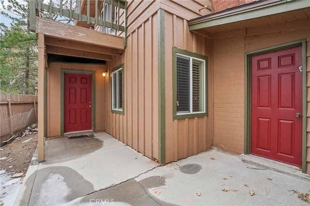 property entrance with board and batten siding, fence, and a balcony