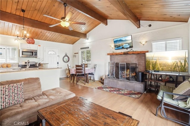 living room featuring light wood finished floors, wooden ceiling, vaulted ceiling with beams, a fireplace, and ceiling fan with notable chandelier