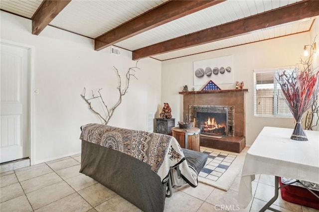 living room with a warm lit fireplace, visible vents, beam ceiling, and light tile patterned floors