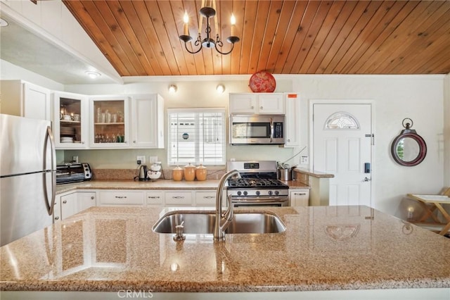 kitchen with white cabinets, glass insert cabinets, light stone countertops, stainless steel appliances, and a sink