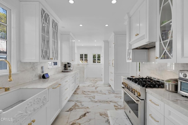 kitchen with light stone countertops, white cabinetry, glass insert cabinets, and stainless steel stove