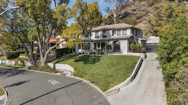 mediterranean / spanish house featuring stucco siding, a tiled roof, and a front yard